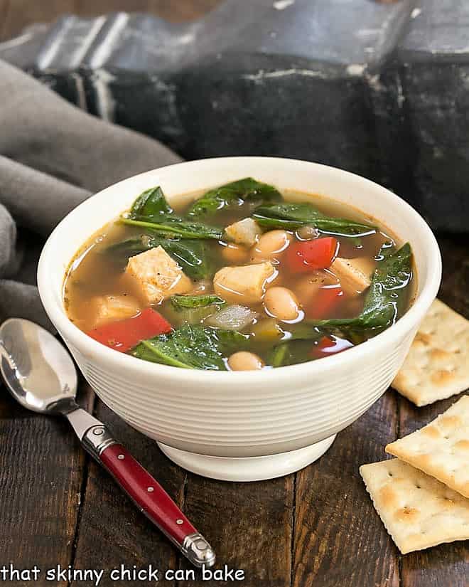 Small white bowl of white chicken chili with saltine crackers and a red handled spoon.