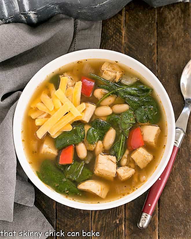 White Chicken Chili in a white ceramic bowl garnished with cheddar cheese and next to a soup spoon.