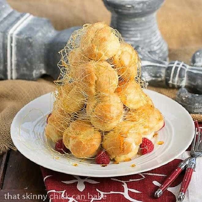 Lemon Cream Croquembouche on a white serving plate garnished with fresh raspberries and spun sugar.