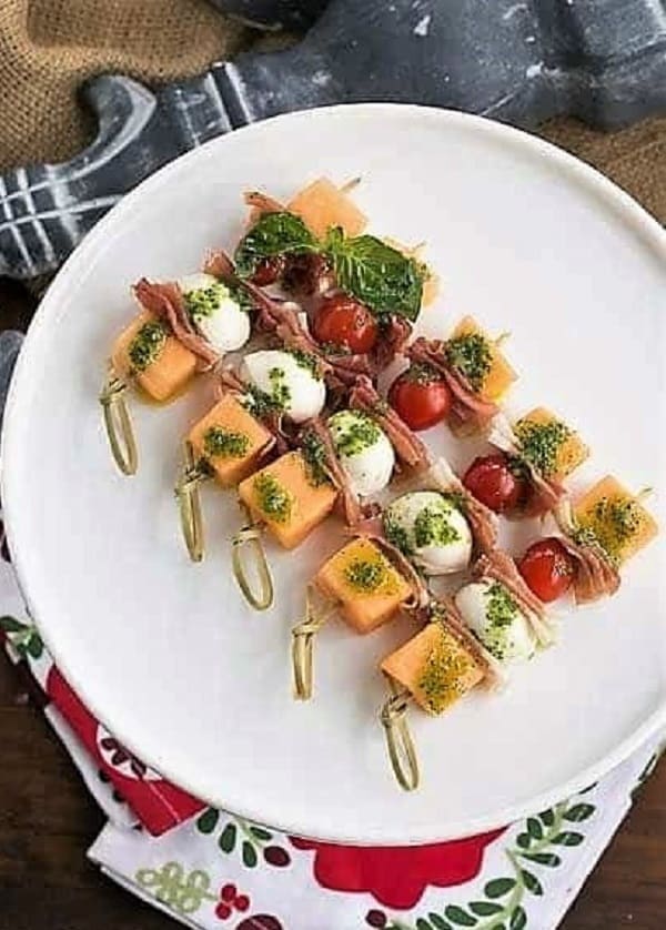 Melon and Prosciutto Skewers lined up on a white cake stand.