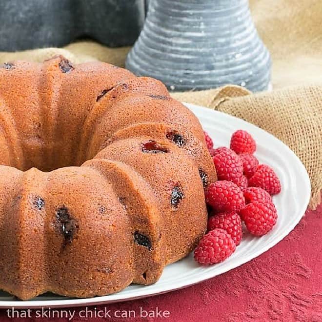 Raspberry Amaretto Bundt Cake on a cake plate with fresh raspberries.