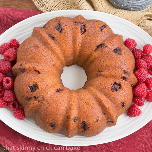 Raspberry Bundt Cake full of fresh raspberries and flavored with extracts and liqueur Overhead view of Raspberry Amaretto Bundt Cake on a white, oval platter.
