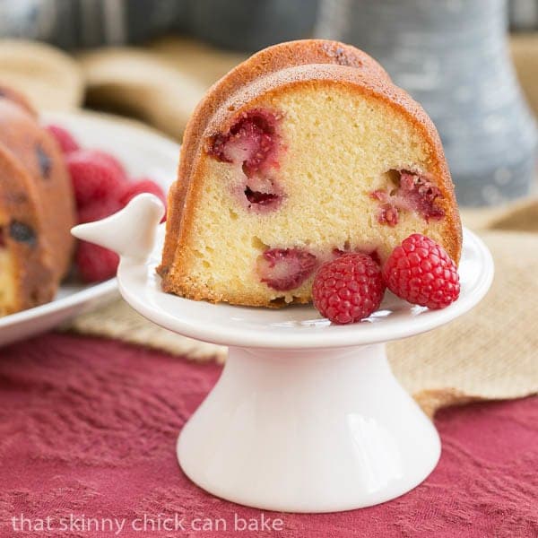 A scumptious Raspberry Pound Cake full of fresh raspberries and flavored with extracts and liqueur Raspberry Amaretto Bundt Cake slice on a small white pedestal.