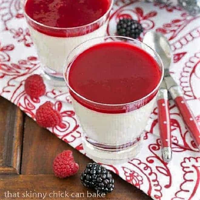 Vanilla Bean Panna Cotta in glasses on a red and white patterned napkin with fresh berries