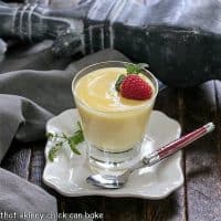 White Chocolate Pudding in a glass topped with a raspberry and mint, on a white plate with a red handle fork