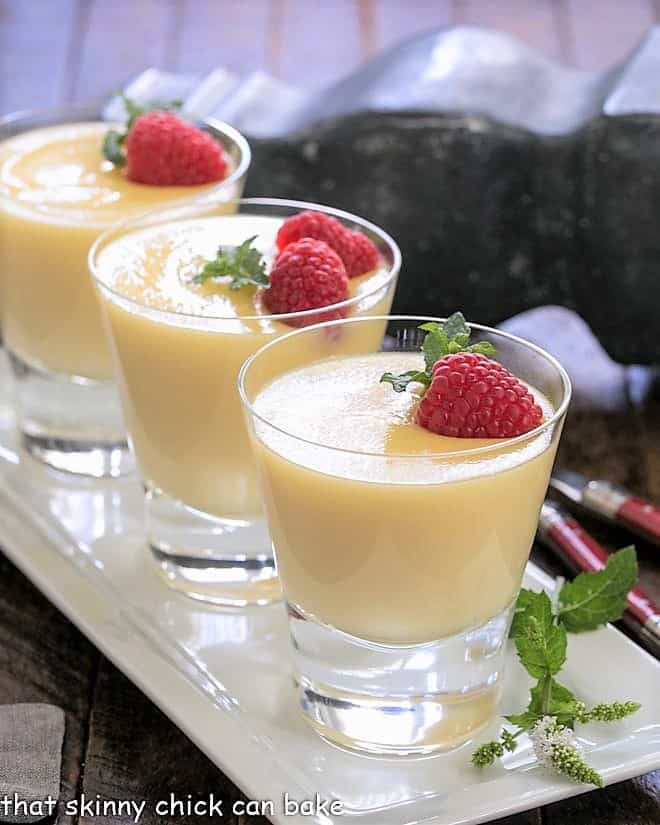 3 glasses of white chocolate pudding on a white tray garnished with fresh raspberries.