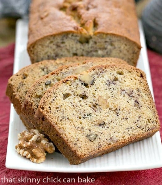 Classic Banana Walnut Bread on a white ceramic tray garnished with walnuts.