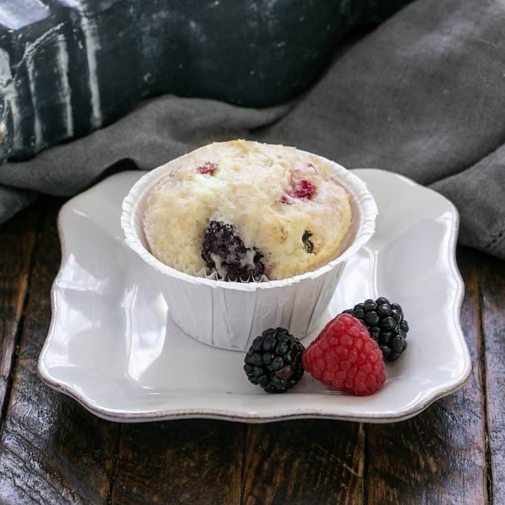 One berry muffin on a small white plate with a berry garnish