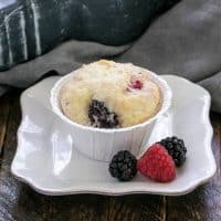 One berry muffin on a small white plate with a berry garnish