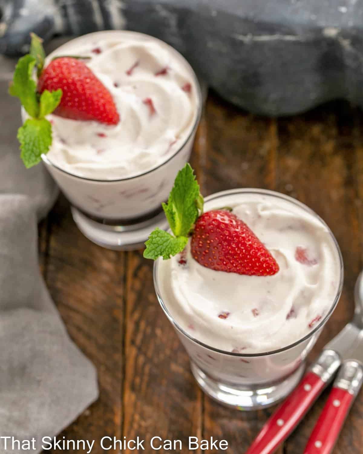 Overhead view of 2 strawberry fools in glass dishes with 2 red handled spoons.