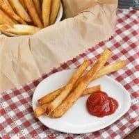 Thin Crispy French Fries on a white plate with a dollop of ketchup
