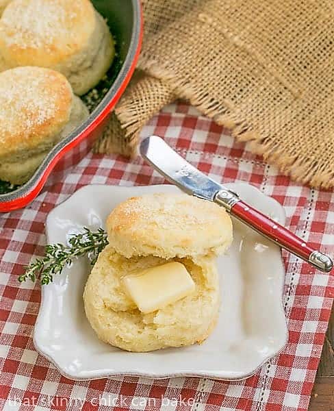 Buttermilk Goat Cheese Biscuits with a pat of butter on a square white plate and a red handle knife.