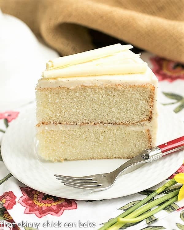 White birthday cake slice on a white plate over a floral napkin.