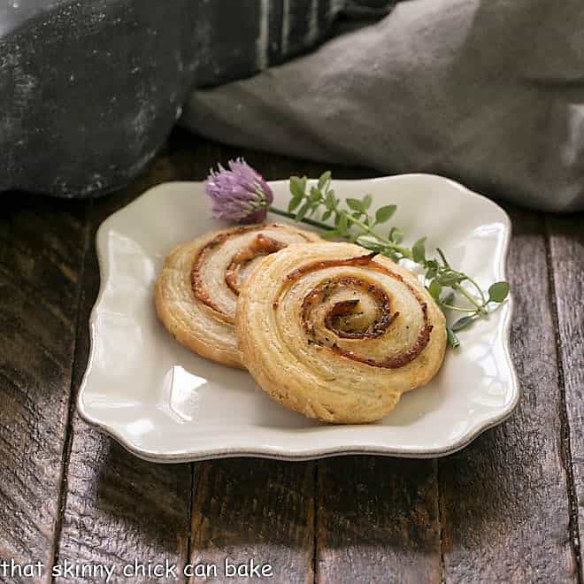 2 pepperoni pinwheels on a square white plate with thyme and chives to garnish