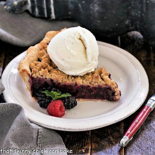 A slice of razzleberry pie with a scoop of vanilla ice cream on a white dessert plate