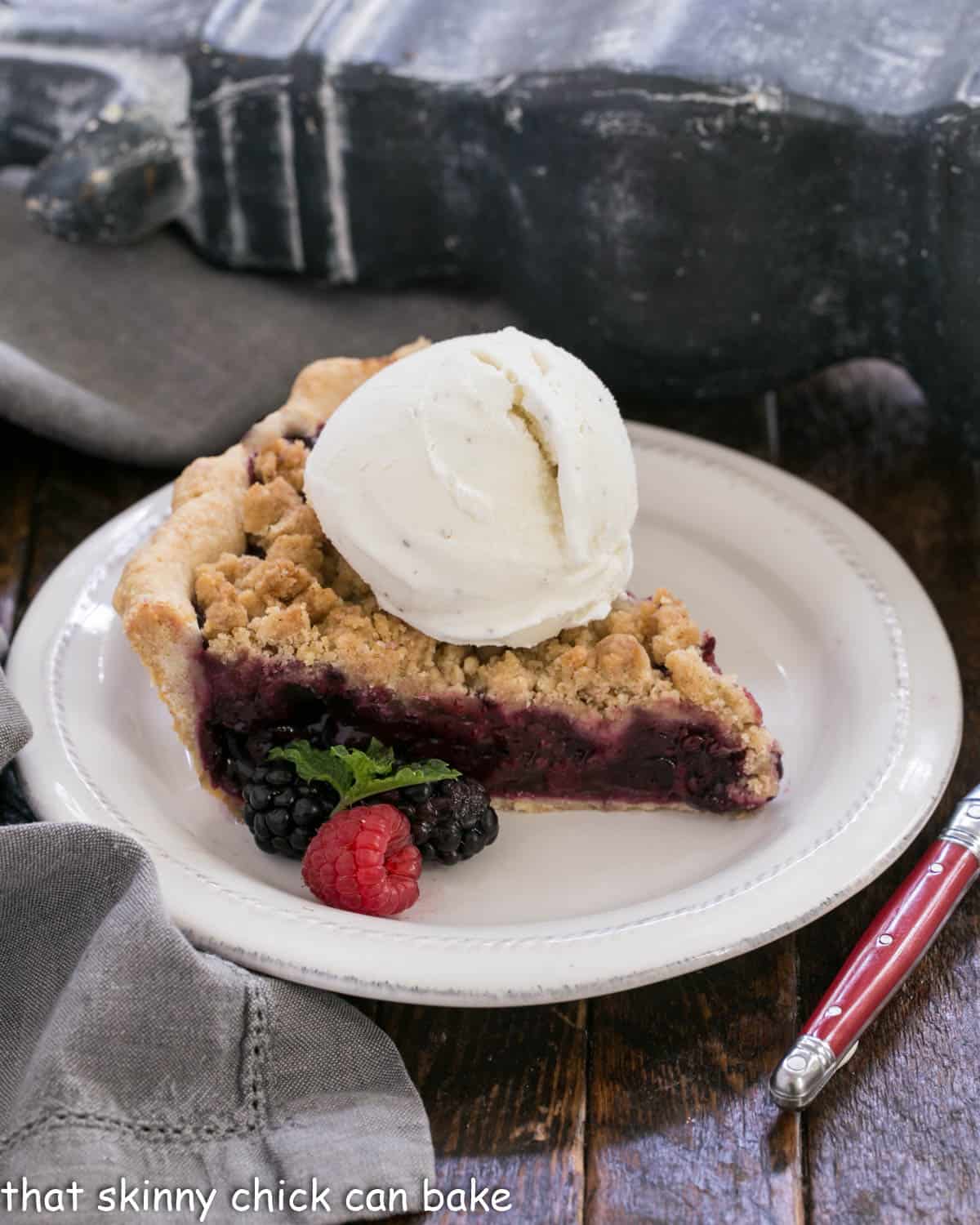 Slice of raspberry pie a la mode on a white dessert plate.