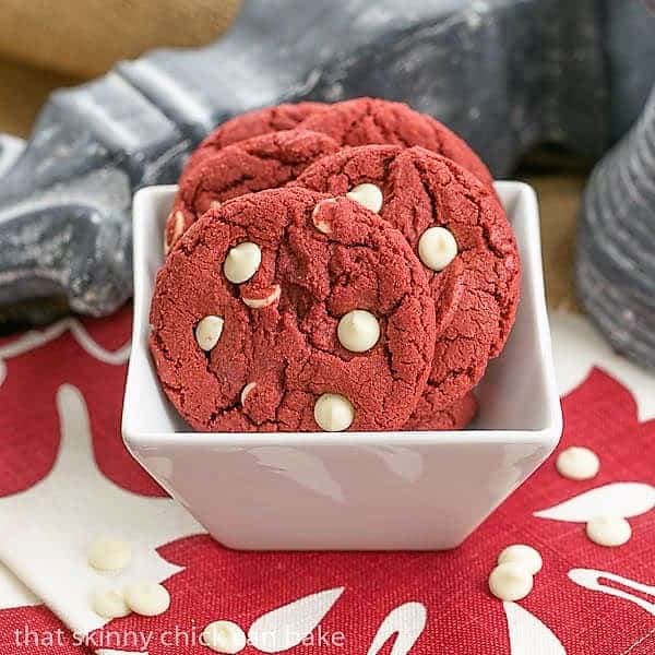 Red velvet cookies with white chocolate chips in a square white bowl.