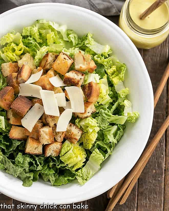 Caesar Salad Recipe from above in a white serving boql with wooden tongs and jar of salad dressing.