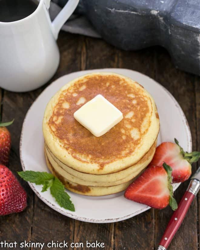 A stack of buttermilk pancakes topped with a pat of butter and served with sliced berries