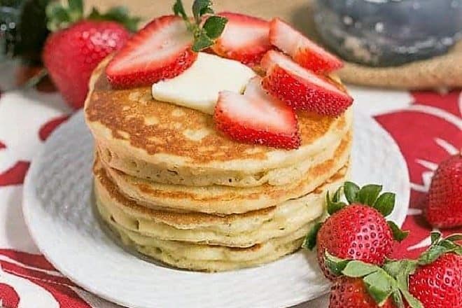 Stack of Classic Buttermilk Pancakes on a white plate topped with strawberries and butter
