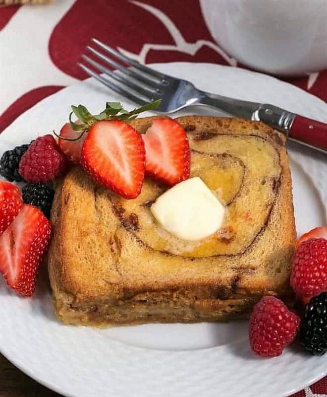 Overnight Cinnamon Bread French Toast on a white plate with a pate of butter and berries.