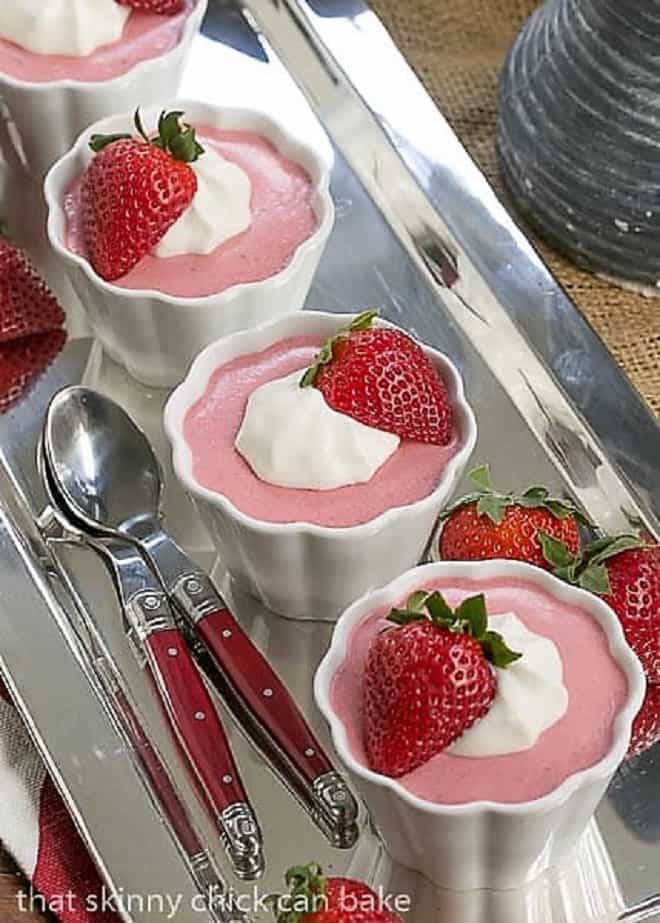 Strawberry Mousse in 4 white ramekins lined up on a silver tray with red handled spoons.