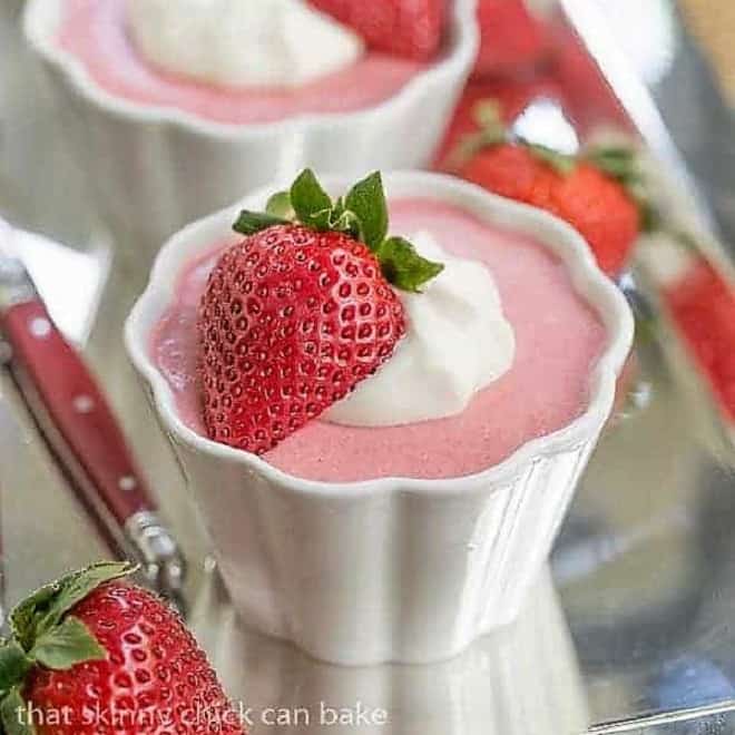 Strawberry Mousse in small white ramekins garnished with whipped cream and half a strawberry.