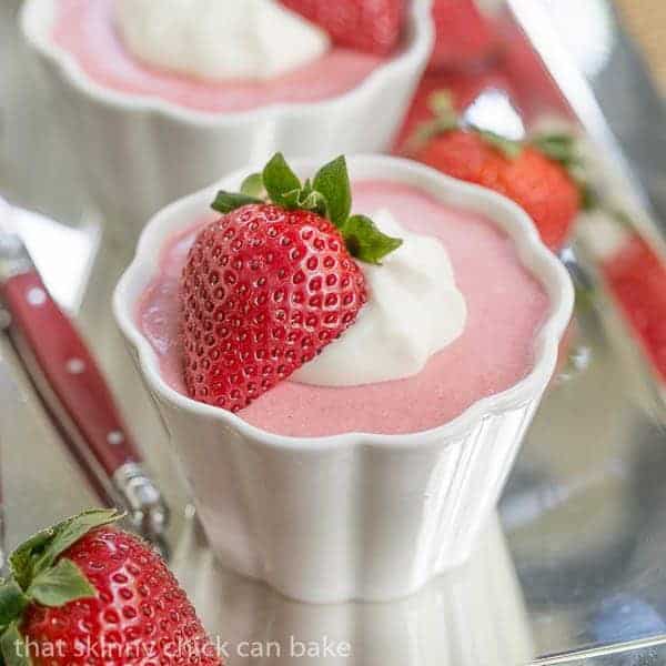 Strawberry Mousse in white ramekins, garnished with a half strawberry and cream on a silver tray