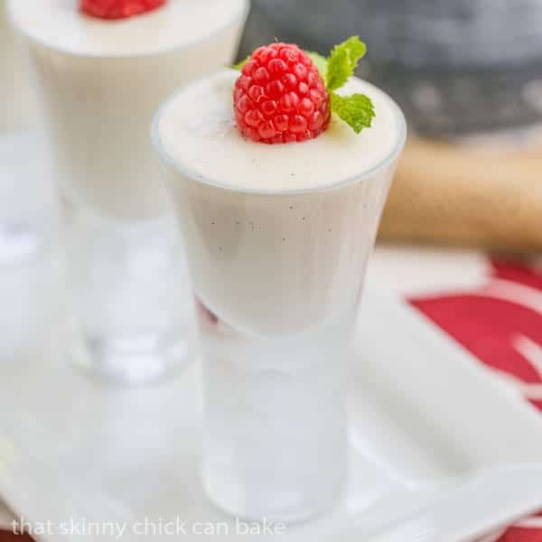 Vanilla Bean Cheesecake Shooters in cordial glasses topped with one raspberry and mint