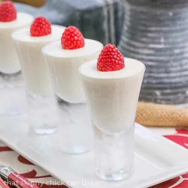 Vanilla Bean Cheesecake Shooters topped with raspberries on a white tray