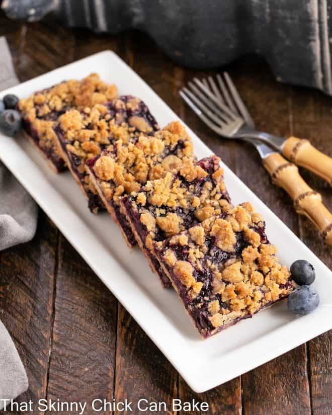 Blueberry streusel bars on a white tray with 2 bamboo forks