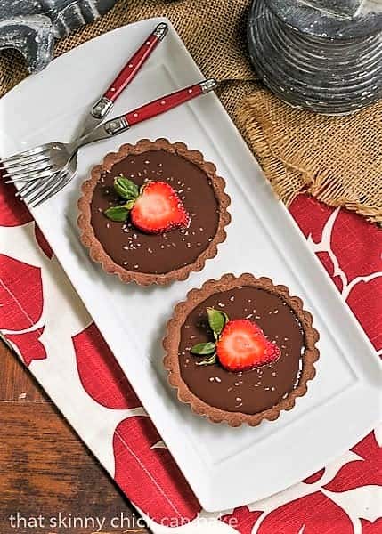 Two Double Chocolate Tartlets on a white rectangular platter with two red handled forks