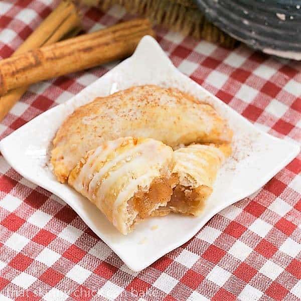 Two Fried Apple Pies on a white ceramic plate on a checkered napkin, with one broken open to expose the filling