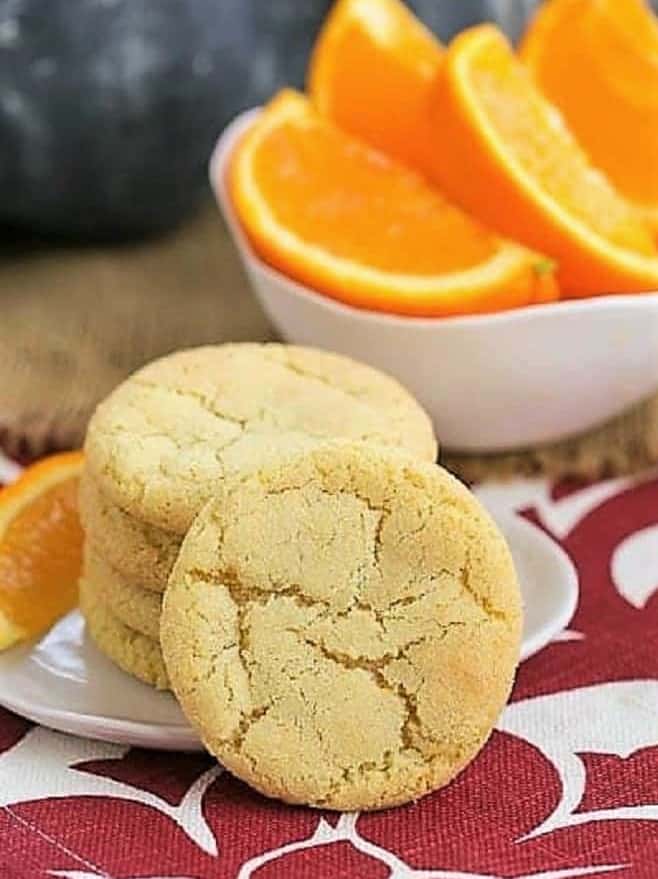 Chewy Orange Crinkles Cookies stacked on a plate with a bowl of orange wedges