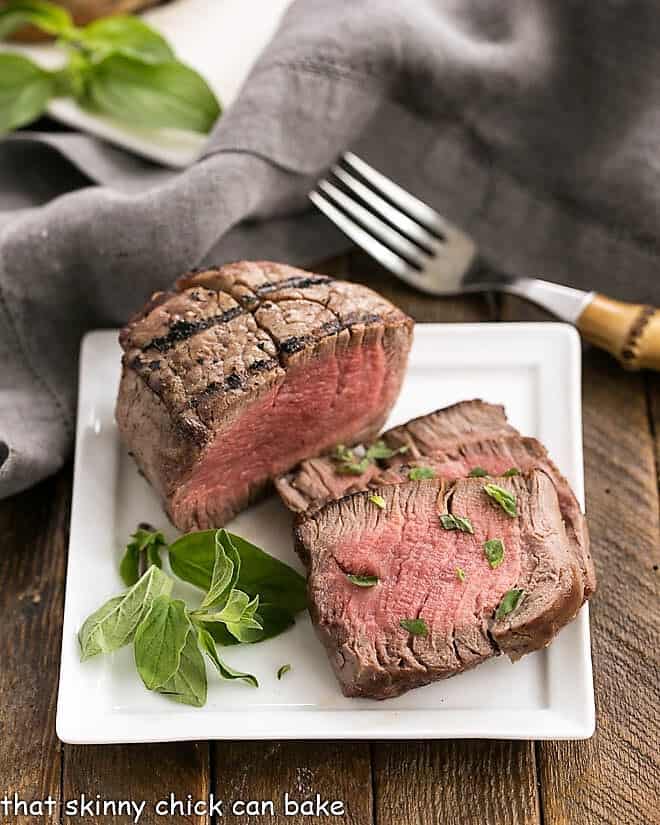 Grilled Steak with Garlic Butter on a square white plate garnished with herbs