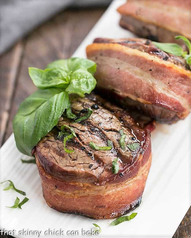 Grilled Steak with Garlic Butter wrapped in bacon on a white platter.