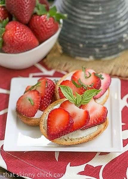 Strawberry Basil Crostini on a white appetizer plate with a bowl of strawberries