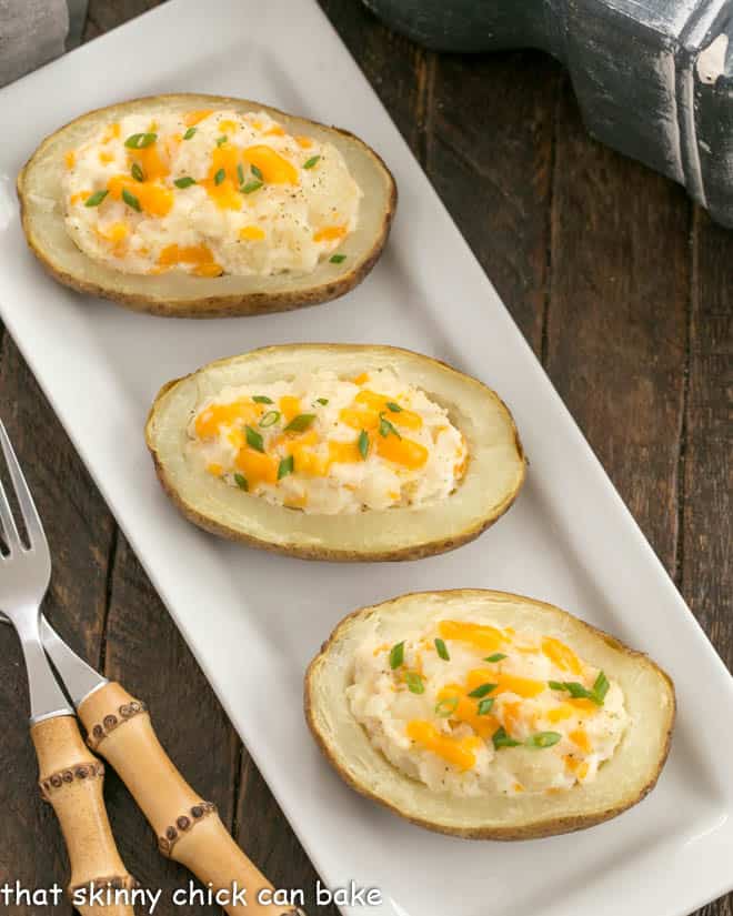 3 twice baked potatos on a white platter with 2 bamboo handled forks.