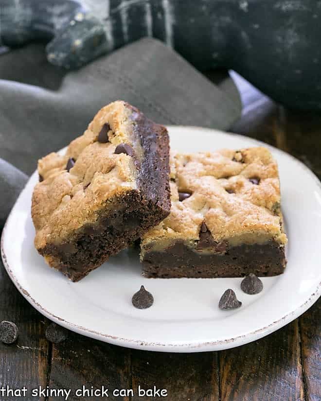 Brookies AKA a Cookies Brownies Recipe - An outrageously rich cookie bar with chocolate chip cookie dough baked over brownie batter! Two brookies stacked on a round white plate with chocolate chips.