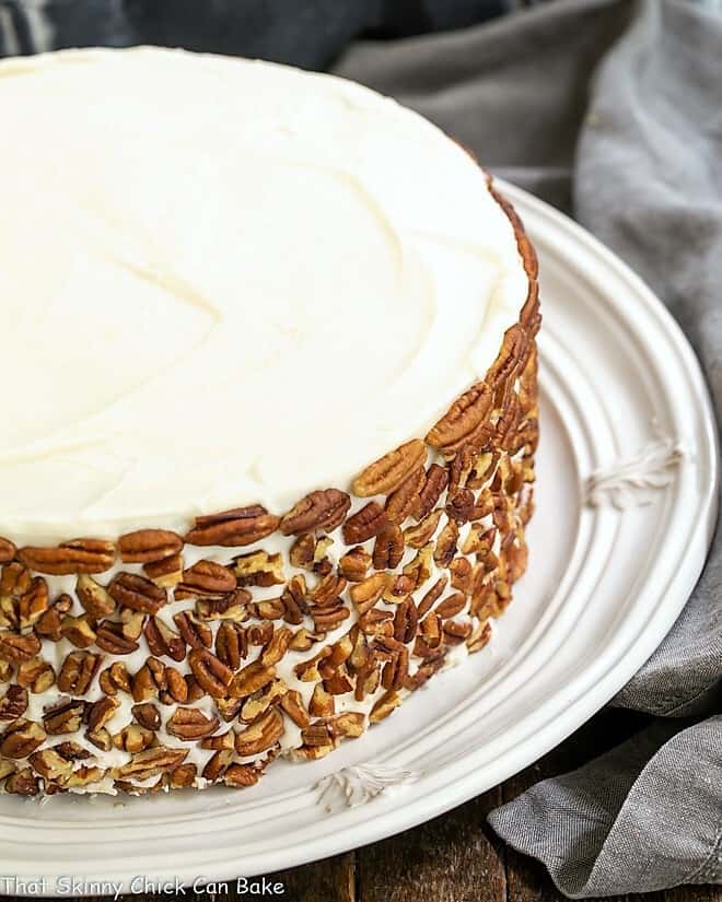 Classic Carrot Cake with pecans on the sides on a white serving plate.