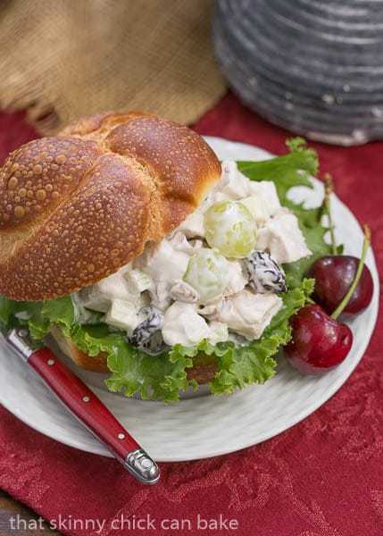 A plate with two cherries, a fork and Chicken Salad on a bun.