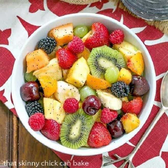 Overhead view of honey lime fruit salad in a white ceramic bowl on a red and white pattern napkin.