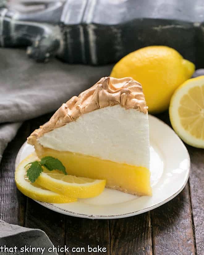 Slice of Mile High Lemon Meringue Pie on a white dessert plate garnished with lemon slices and mint sprigs
