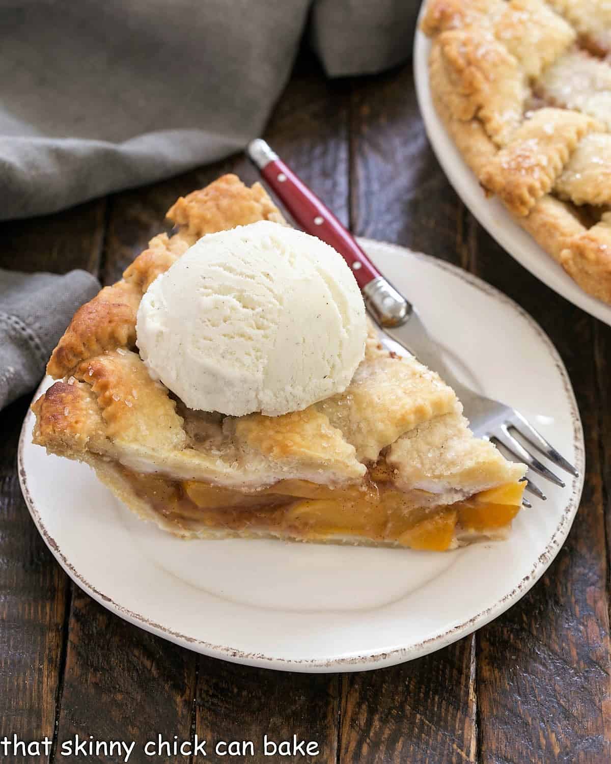 A slice of Peach Pie on a white plate with a scoop of ice cream.