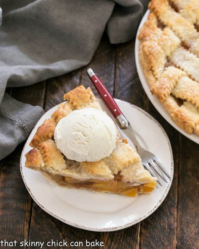 Slice of peach pie on a dessert plate with a red handled fork.