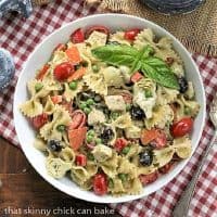 Overhead view of pesto pasta salad in a white bowl on a red and white checked napkin