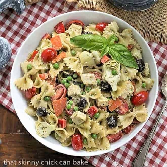 Overhead view of pesto pasta salad in a white bowl on a red and white checked napkin