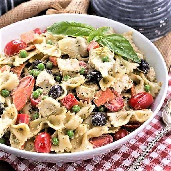 Pesto Pasta Salad in a flat white serving bowl with a silver serving spoon