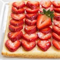 Cheesecake bars topped with strawberries on a white tray