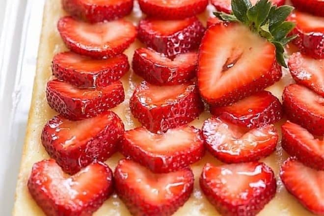 Cheesecake bars topped with strawberries on a white tray